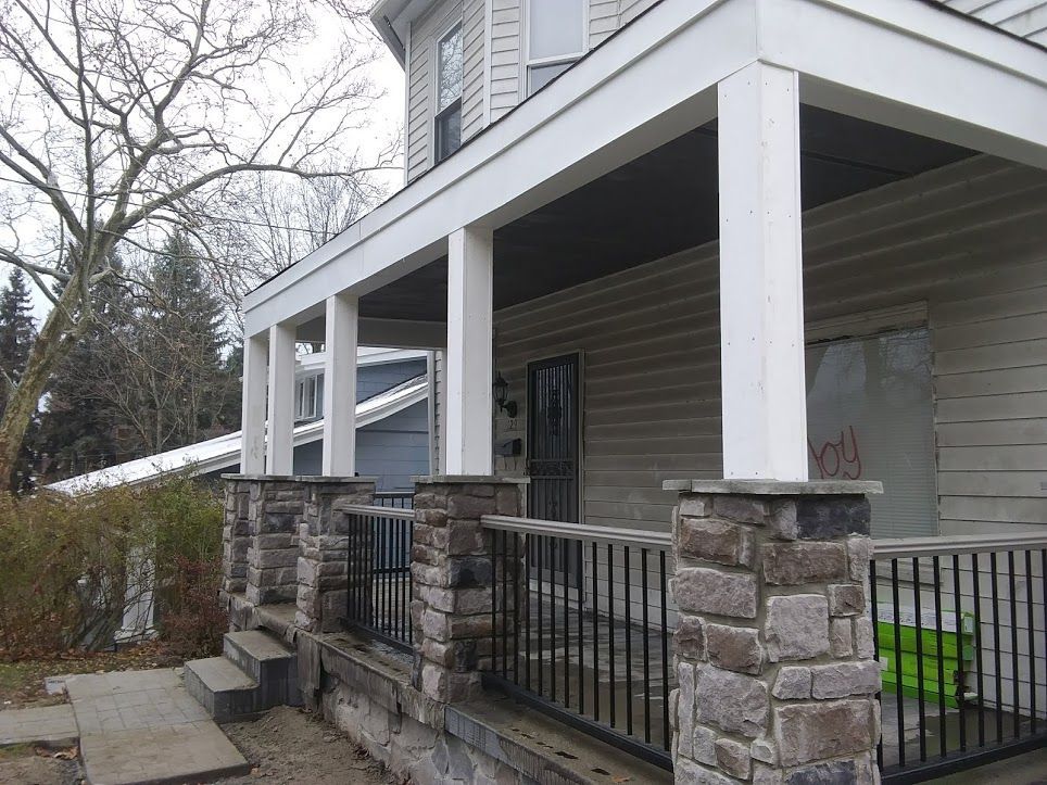 Stone porch with white columns and black railing on a house exterior