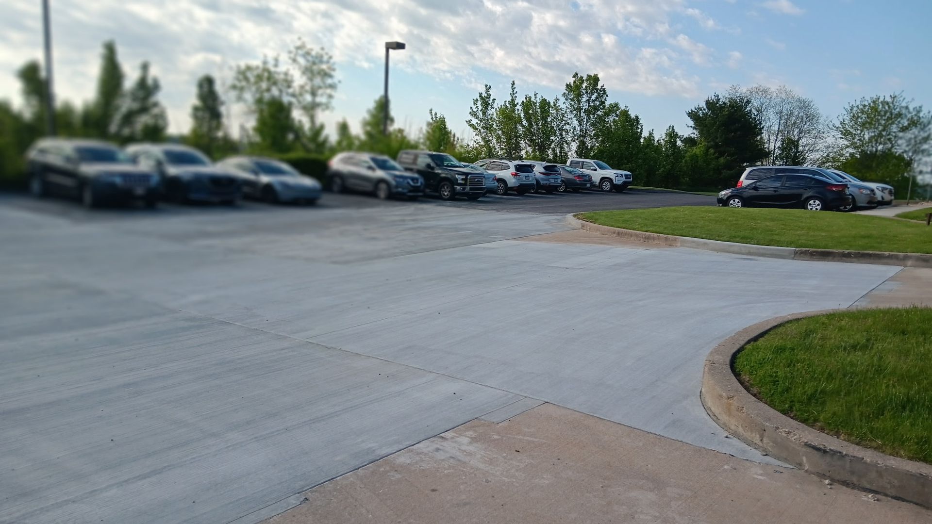 Parking lot with several parked cars beside a concrete drive and grassy curb at sunset