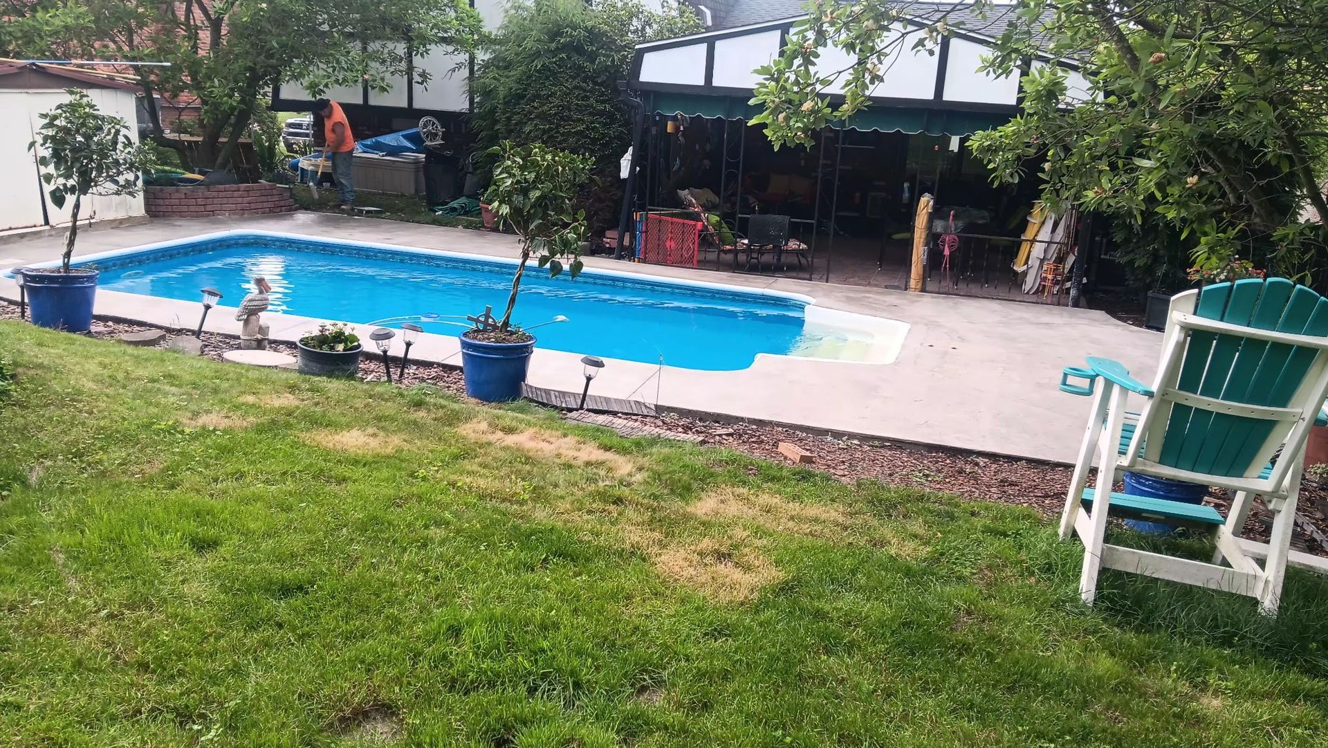 Backyard pool with a small dog, lawn chairs, and a shaded patio in the background