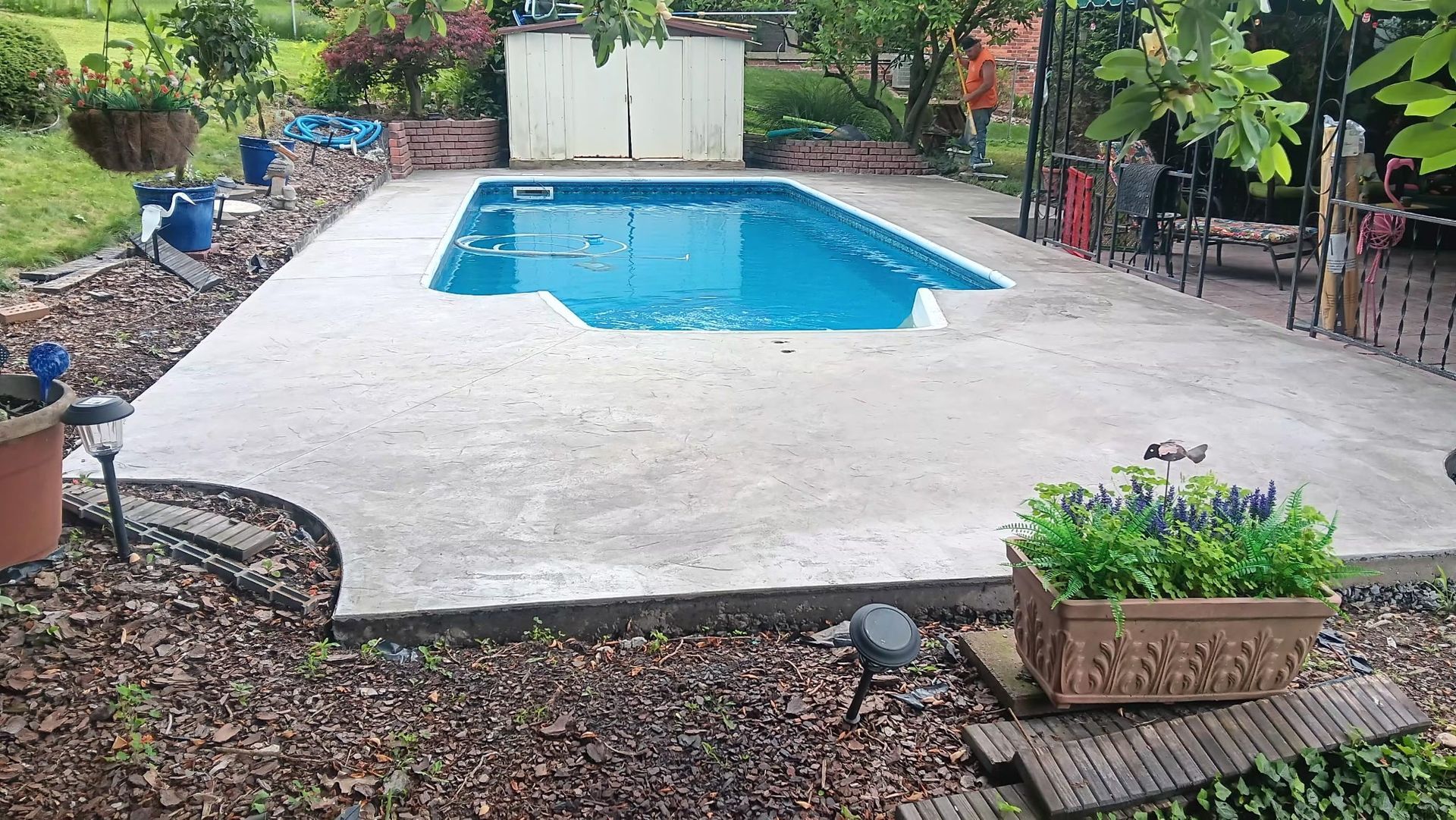 Backyard patio with an in-ground pool, concrete deck, and flower planters