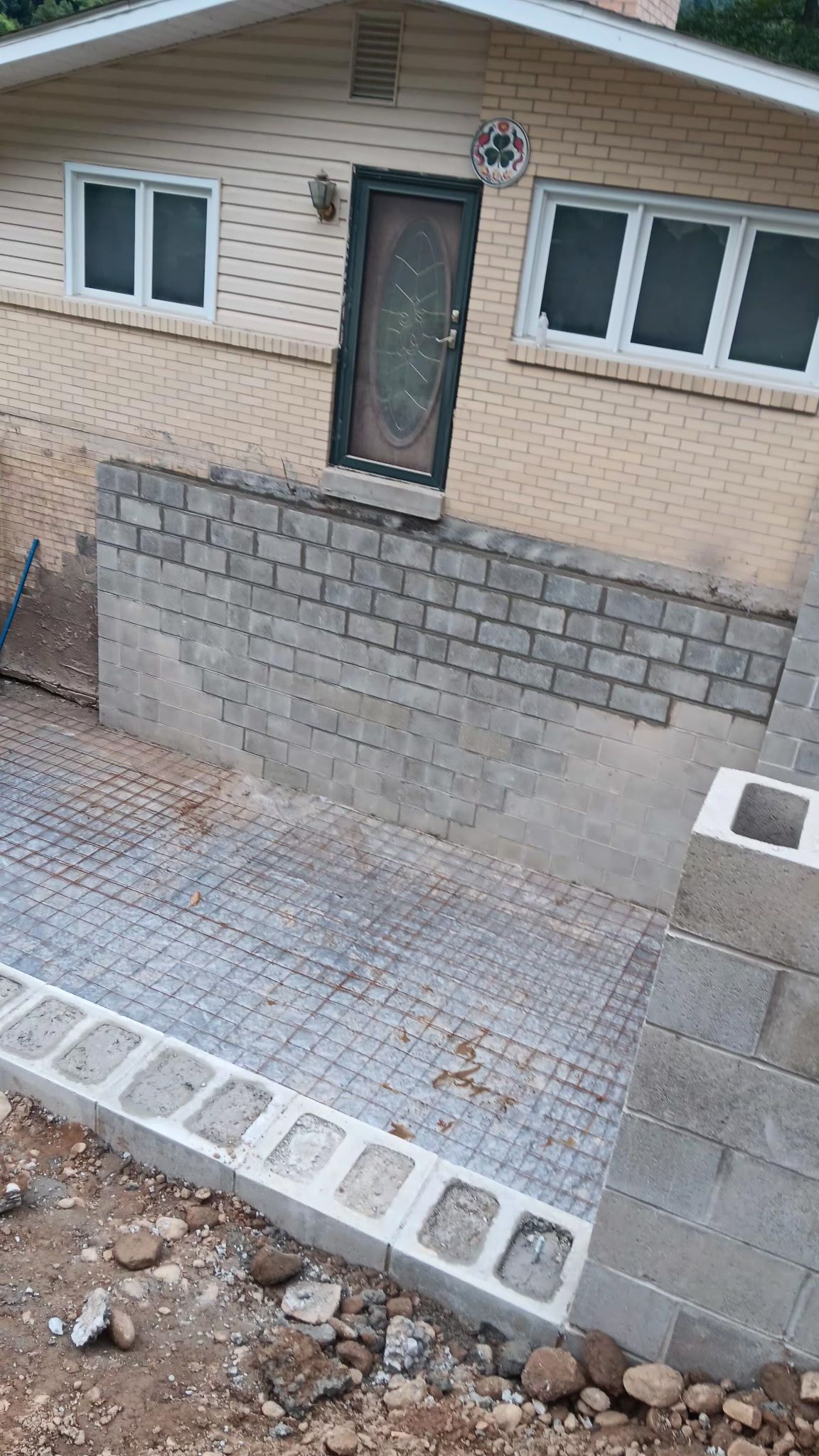 Small brick courtyard and retaining wall in front of a beige house with a dark front door and windows.