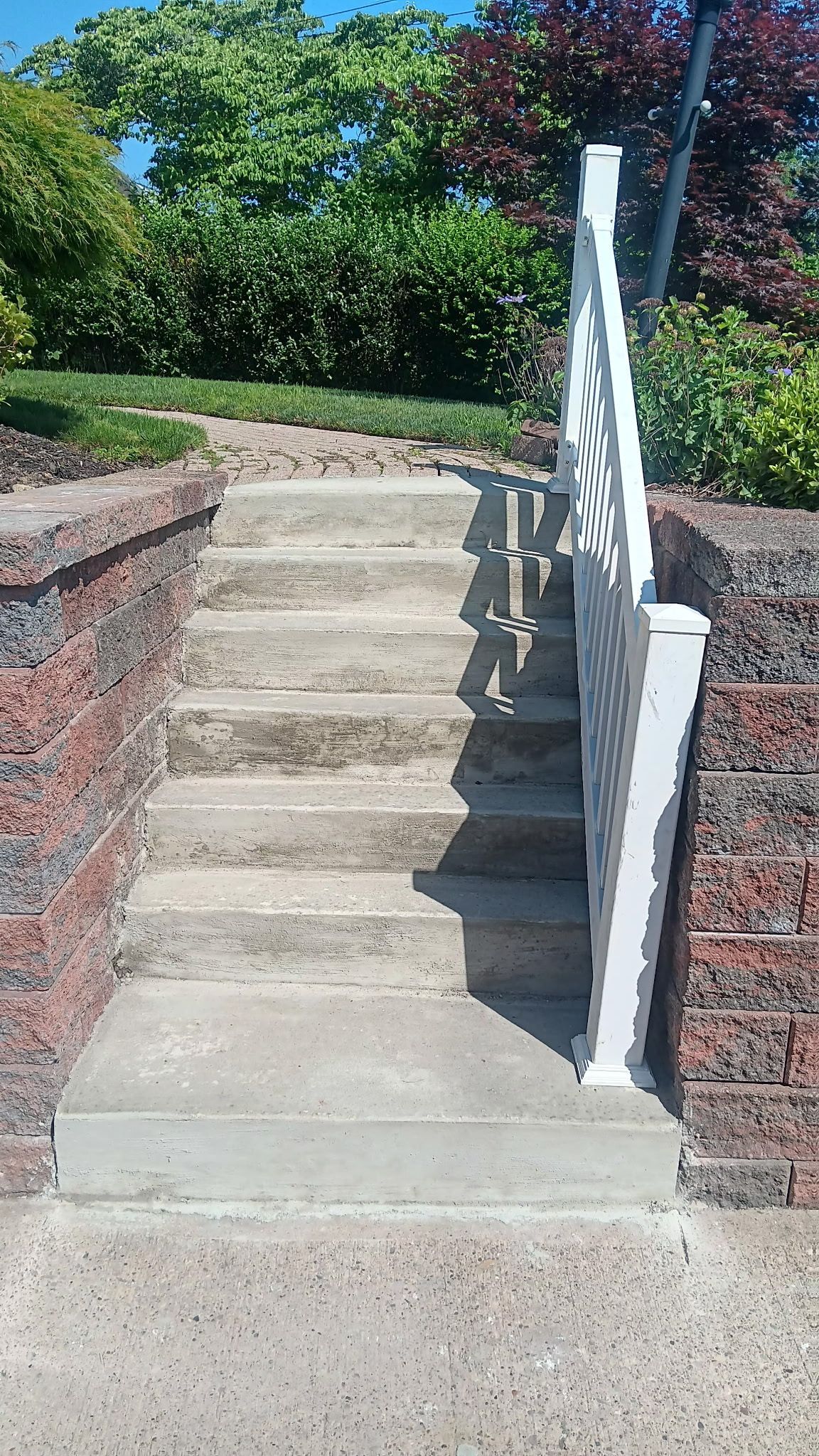 Concrete stairs with white handrail between brick walls and green shrubs on a sunny day