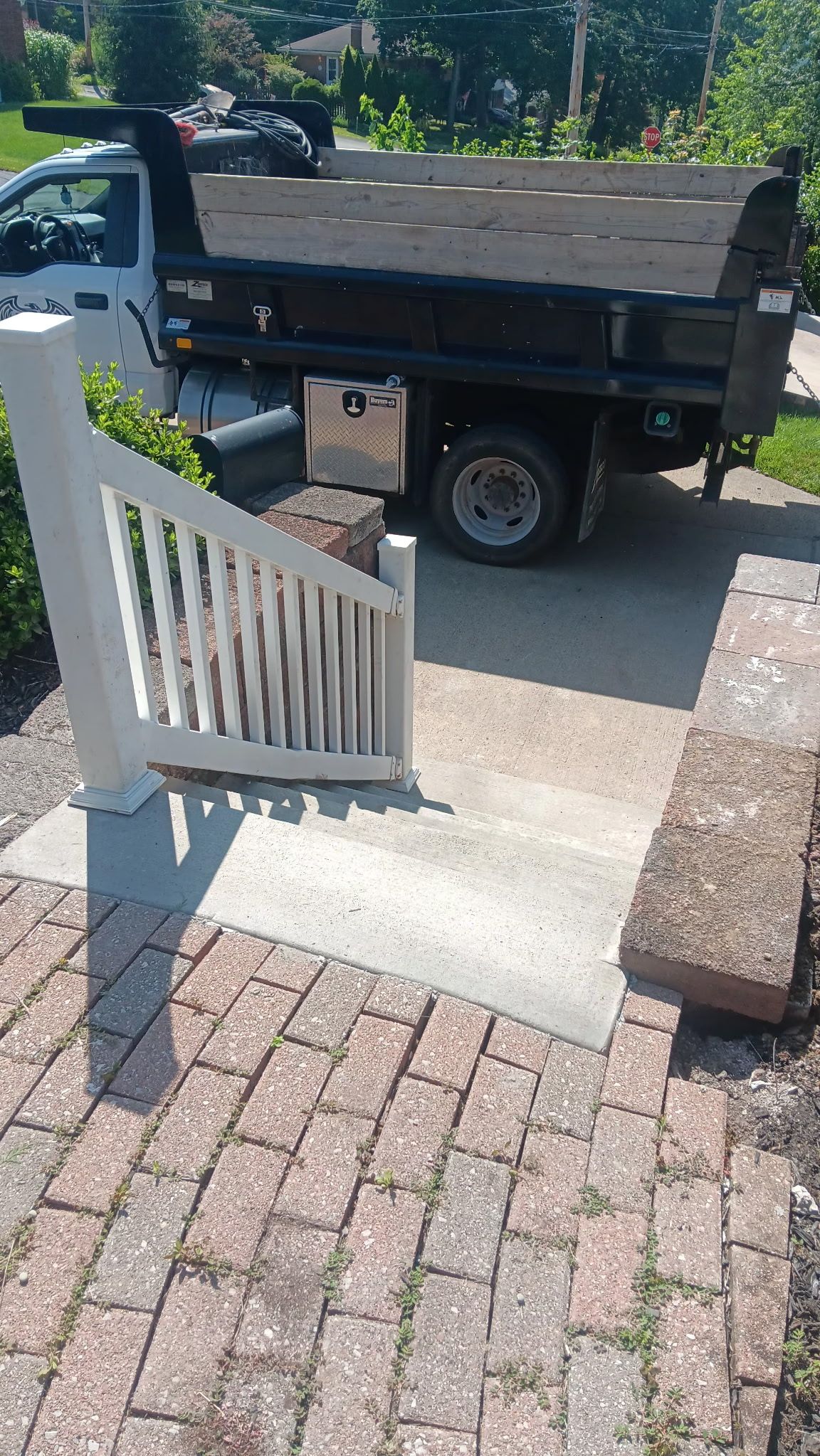 Black utility truck parked beside a white railing and brick walkway in a sunny yard