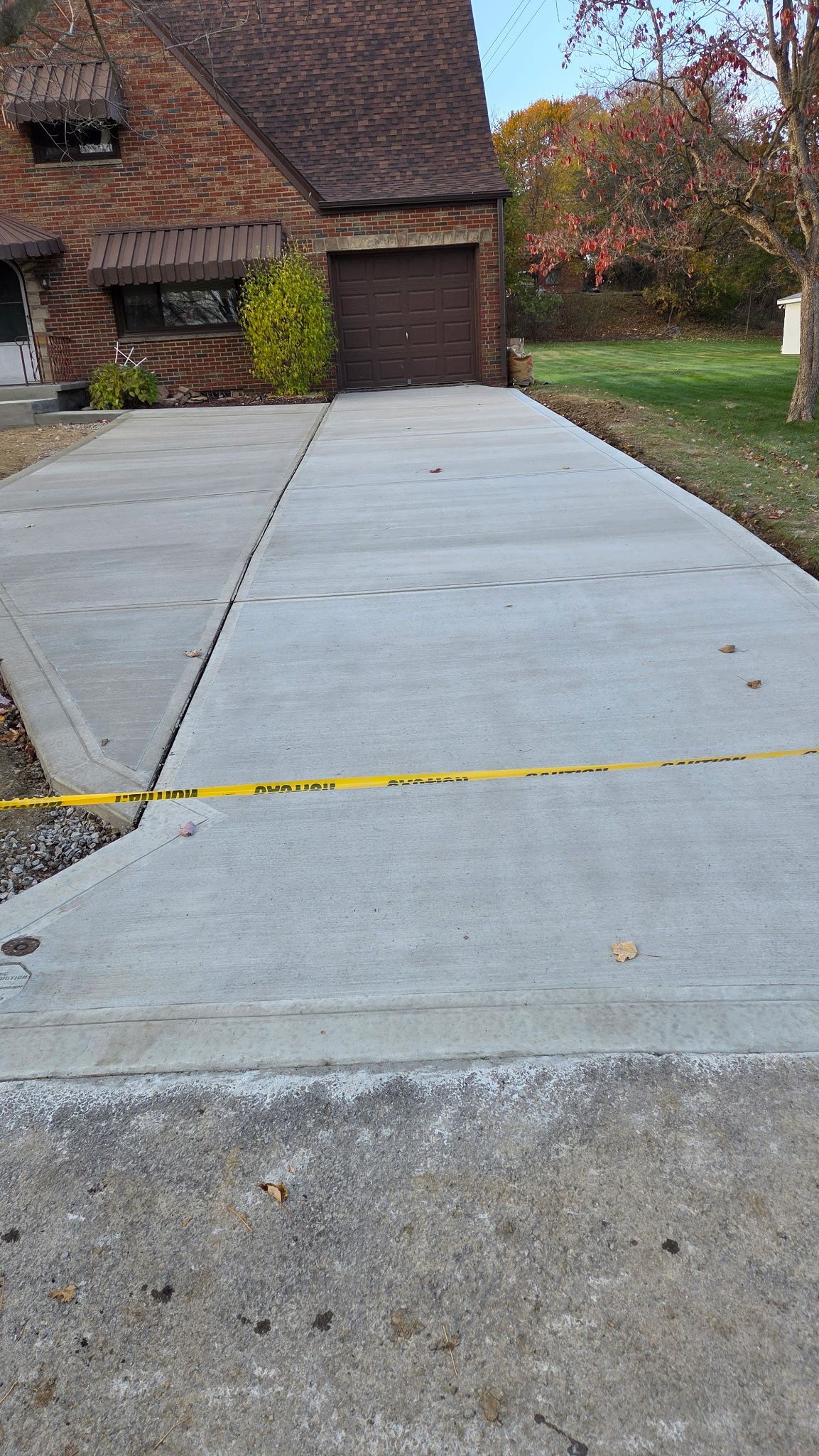 Concrete driveway in front of a brick house, with a yellow caution tape across the bottom edge.