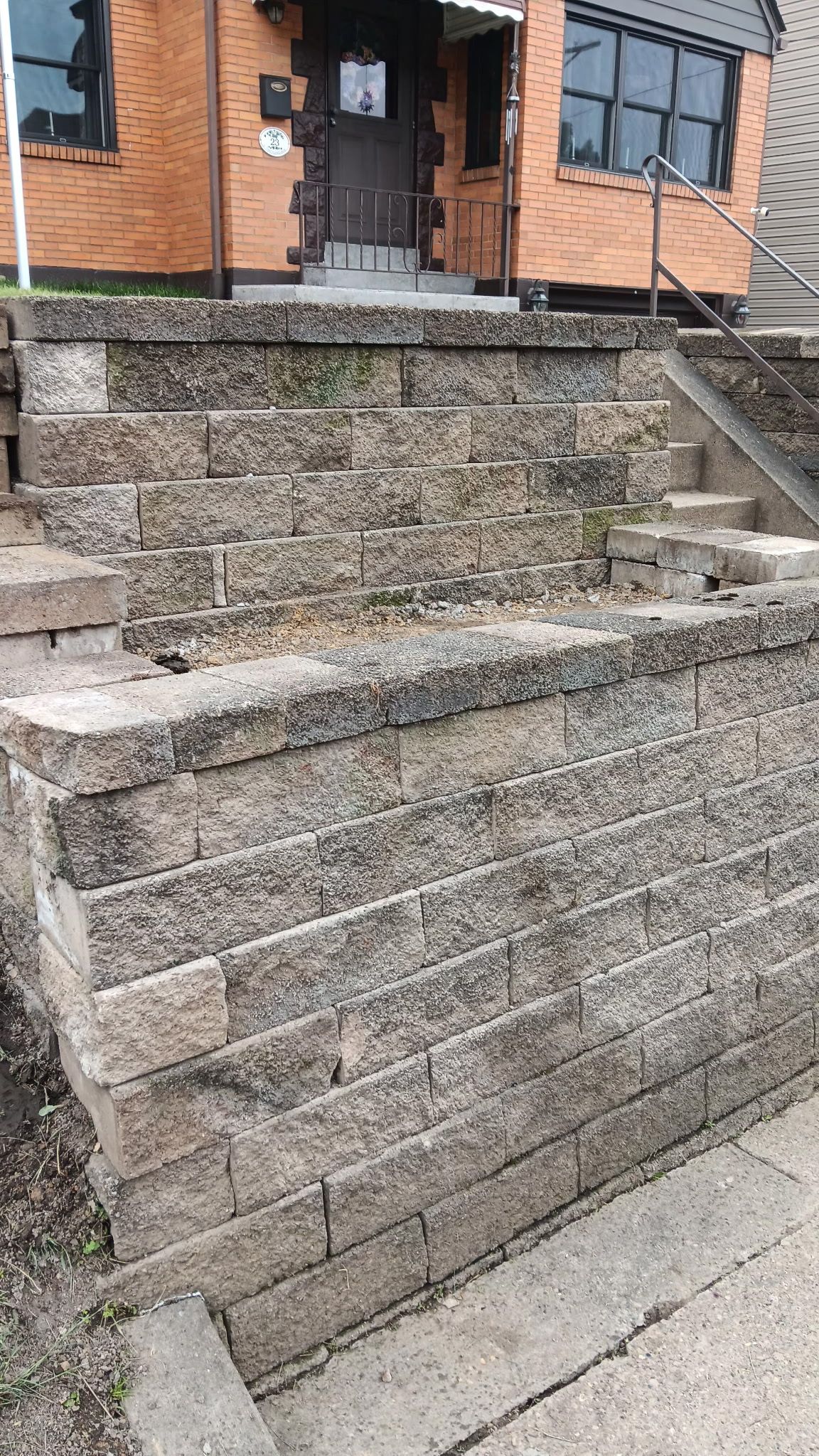 Stone steps leading to a brick building entrance, with a metal handrail on the right
