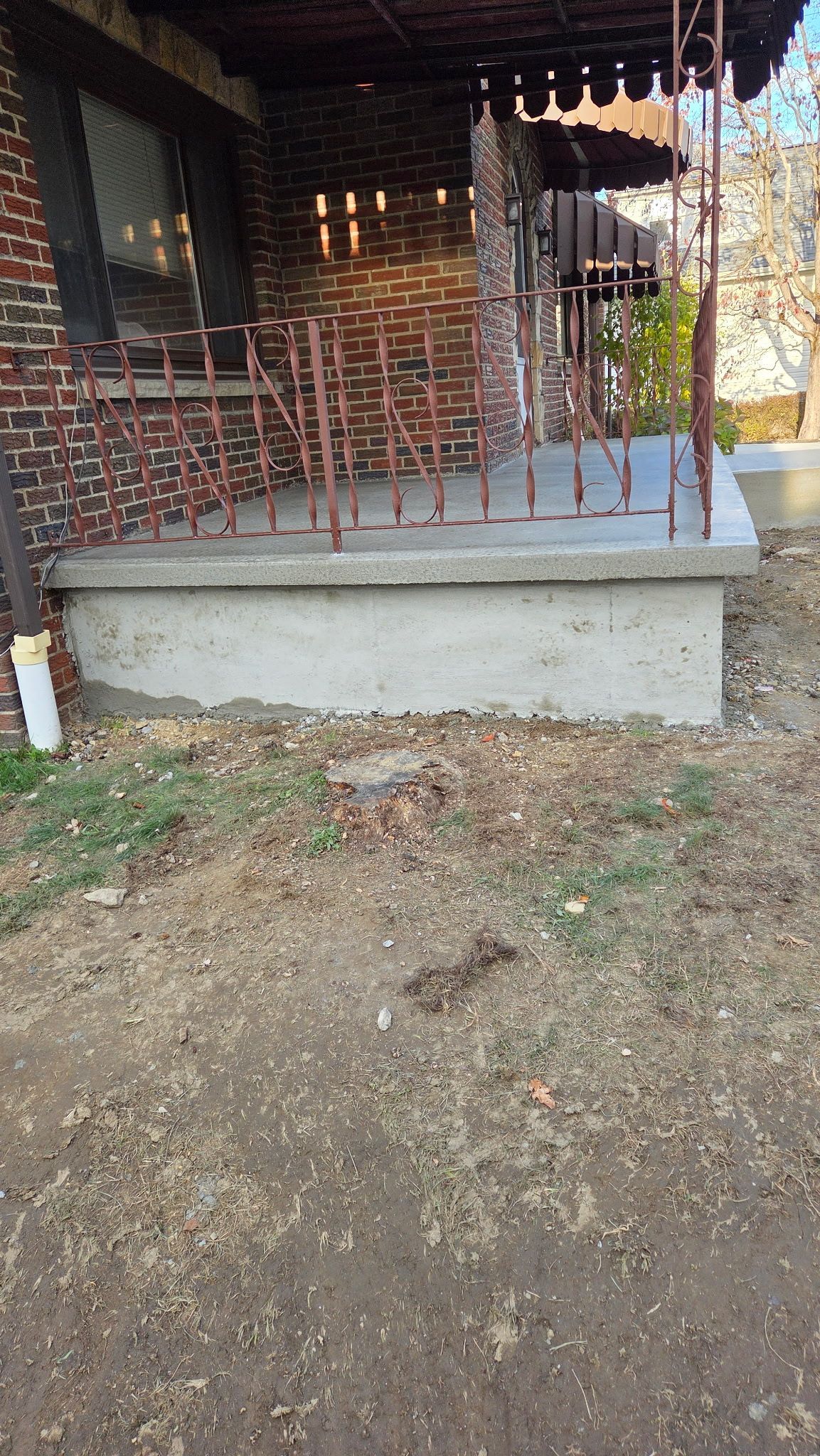 Concrete porch with red railing in front of a rustic wooden house and dirt yard