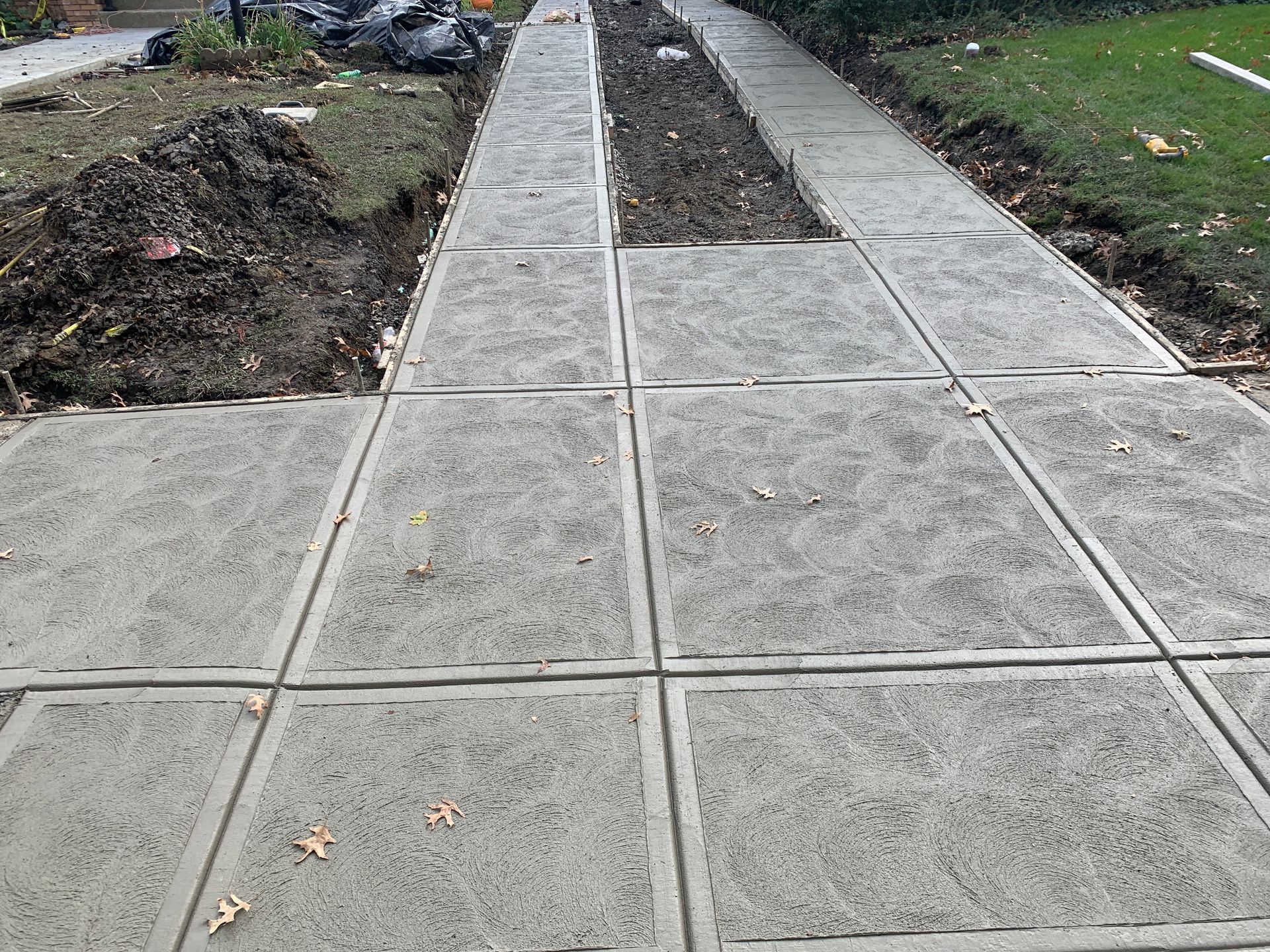 Concrete sidewalk beside bare dirt landscaping beds in a neighborhood.
