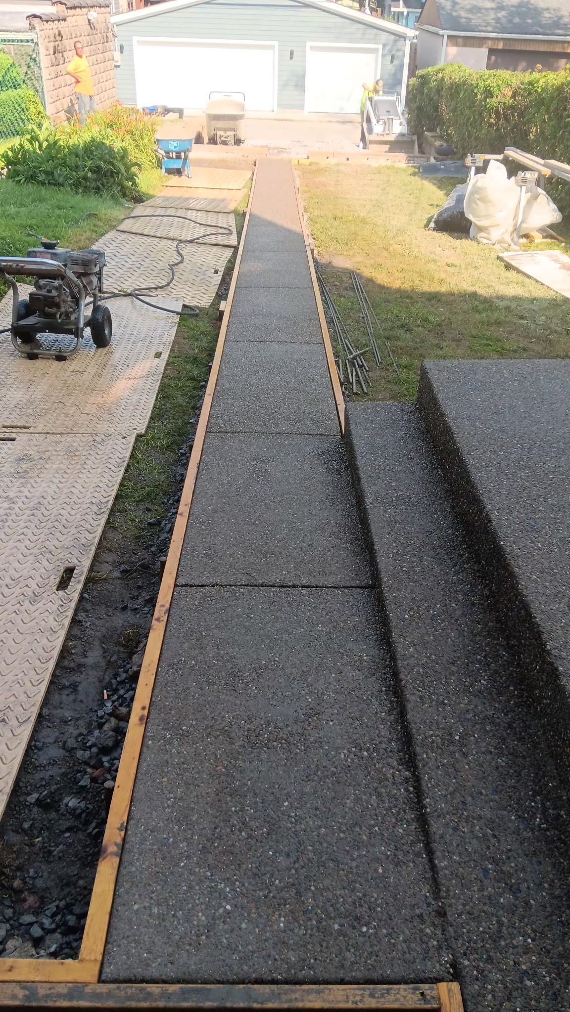 Narrow black walkway under construction in a backyard leading to a white garage.