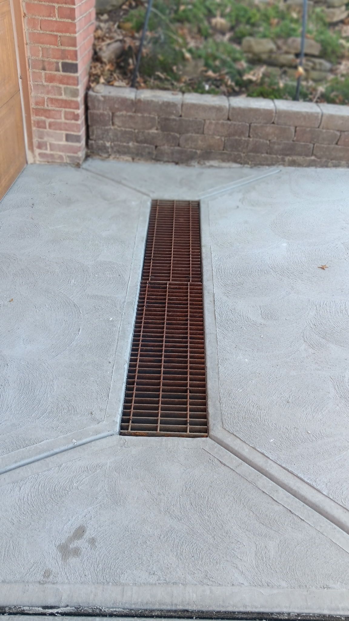 Concrete walkway with a narrow metal drainage grate leading to a brick planter wall