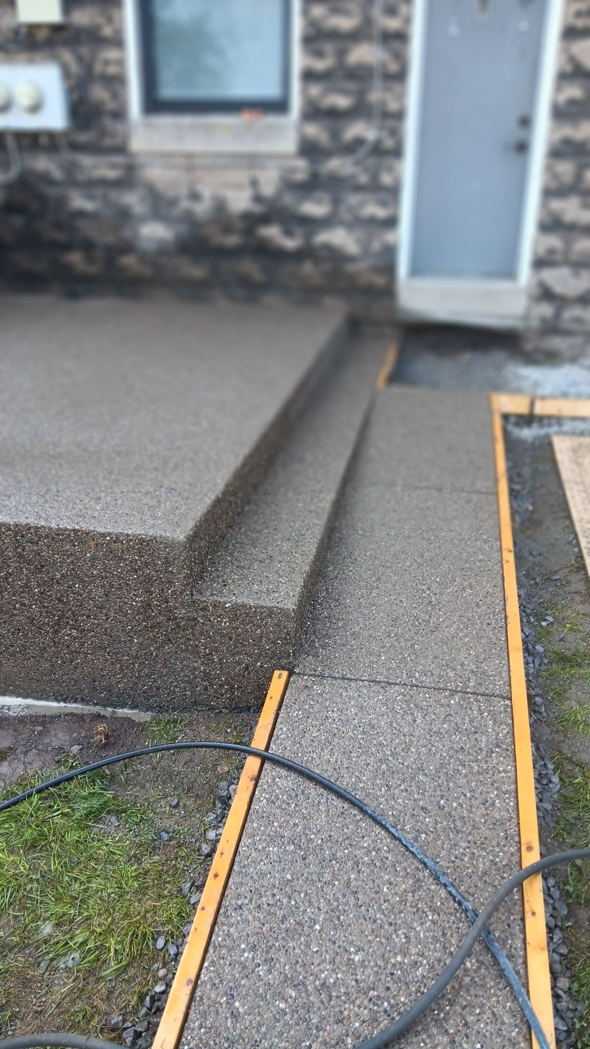 Concrete walkway beside stone house entrance with ramp and yellow edging strips