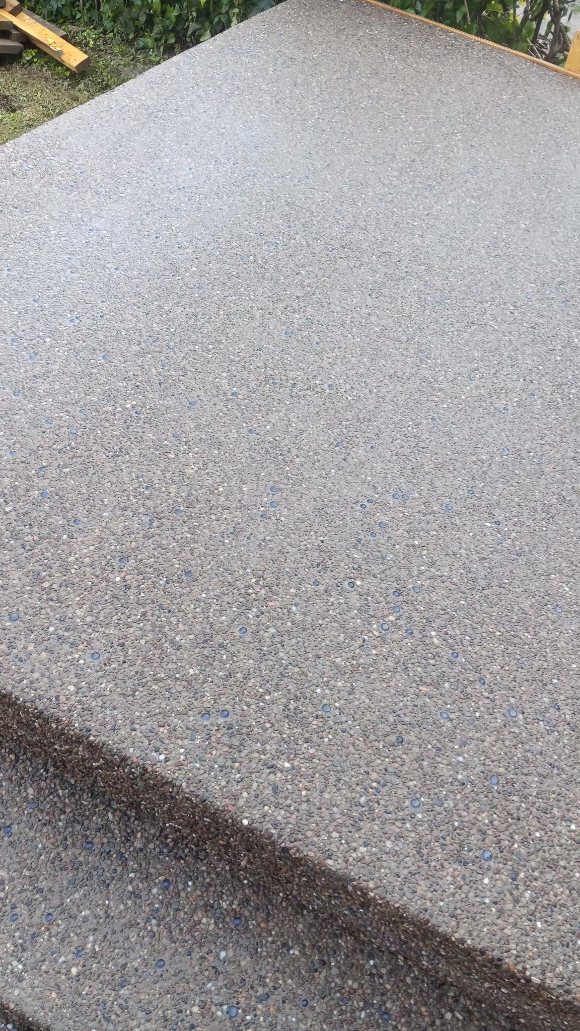 Close-up of a gray speckled stone or concrete surface with a beveled edge outdoors.