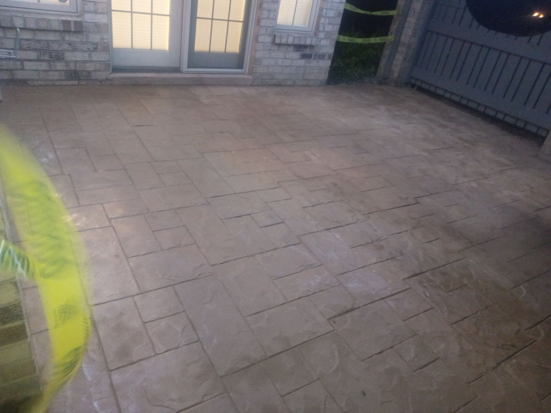 Empty stone patio in front of a glass door, with a metal fence on the right.