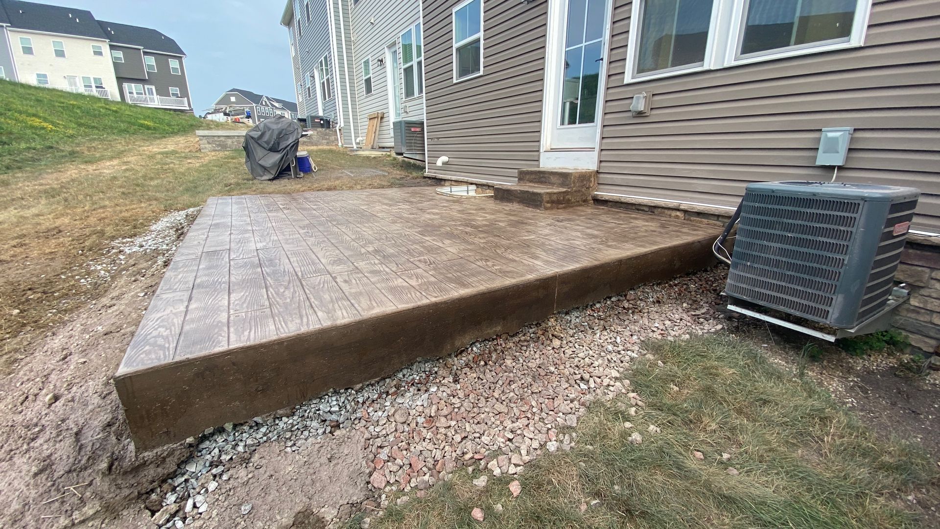 Backyard wooden deck beside a house, with an air conditioner unit and gravel below.