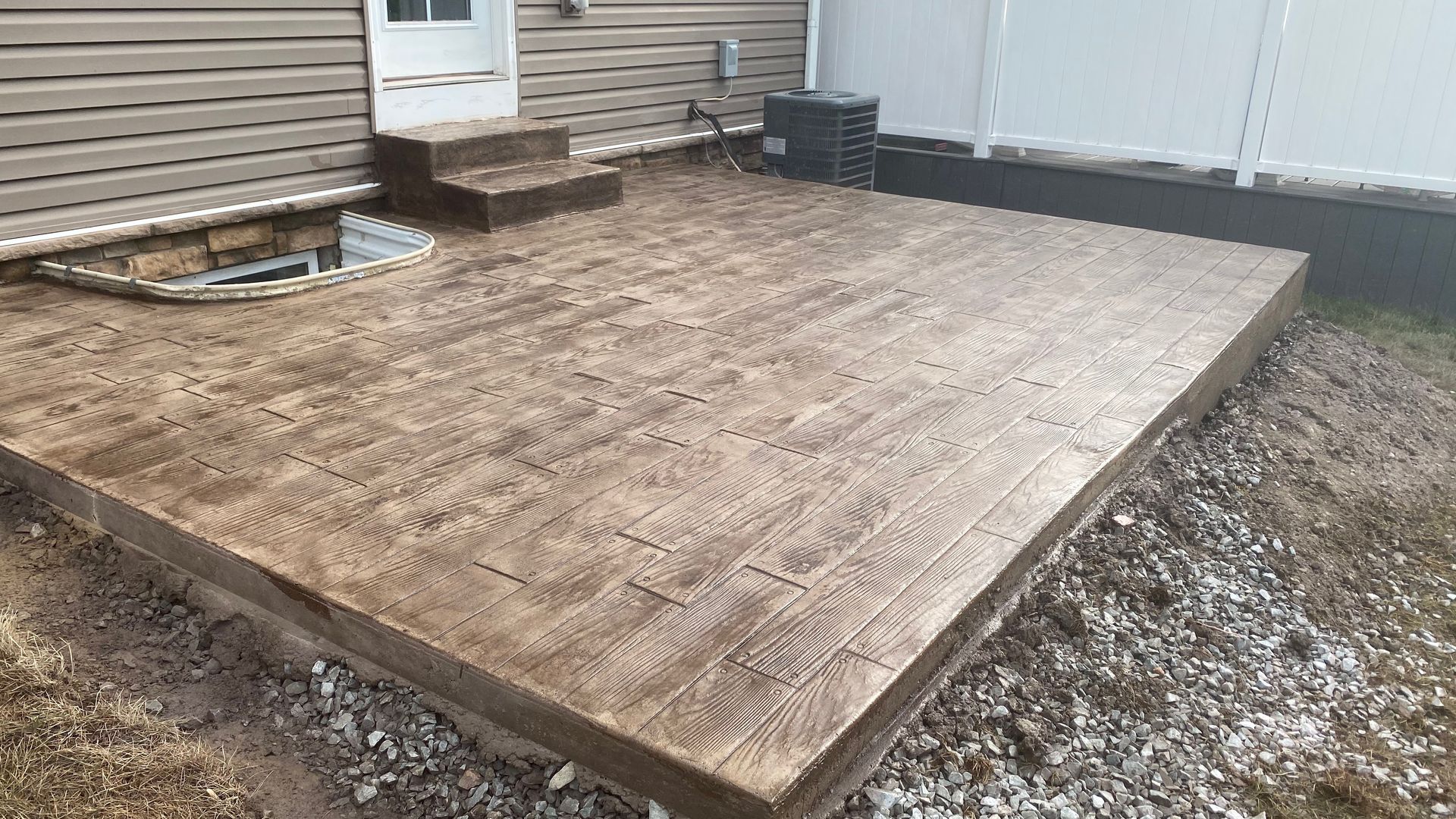 Wooden backyard deck under construction beside a house, with a white door and steps.