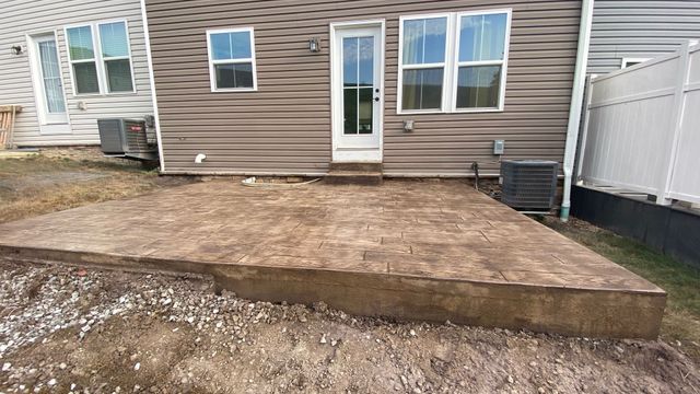 Backyard concrete patio with a white door, windows, and a gravel yard