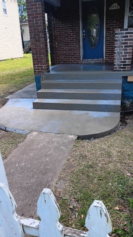 Front porch with gray concrete steps, blue door, and a curved walkway leading to a small white fence.