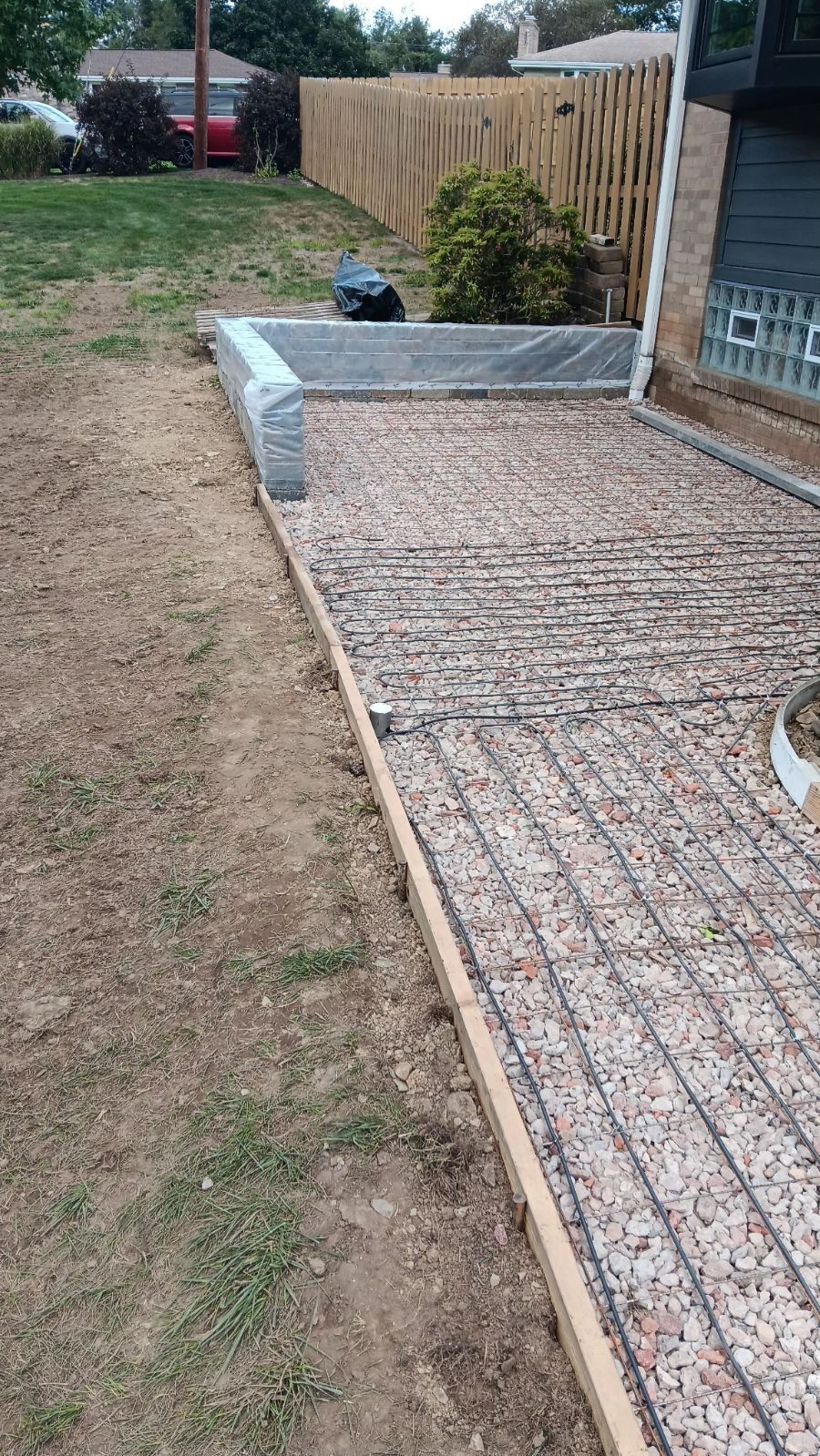 Backyard patio with gravel and concrete edging beside a grassy lawn and wooden fence