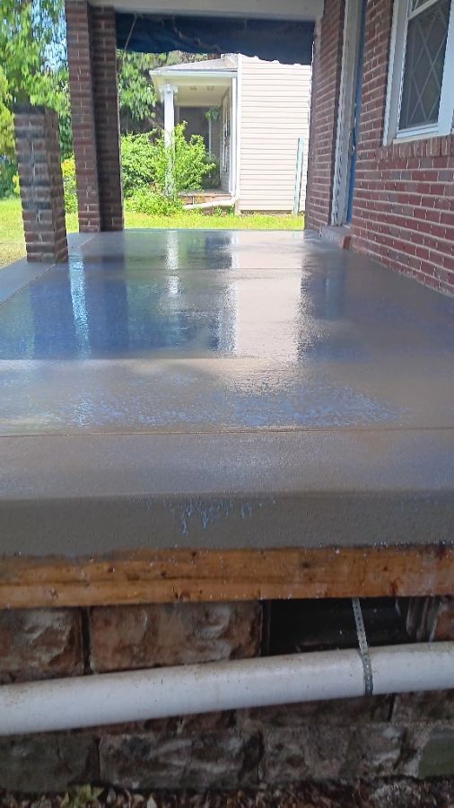 Fresh concrete porch beside a brick house, with a view toward a backyard and a white outbuilding.