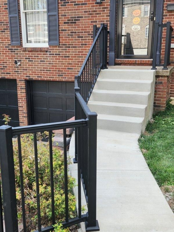 Brick townhouse entrance with concrete steps, black railing, and basement walkway to a side door