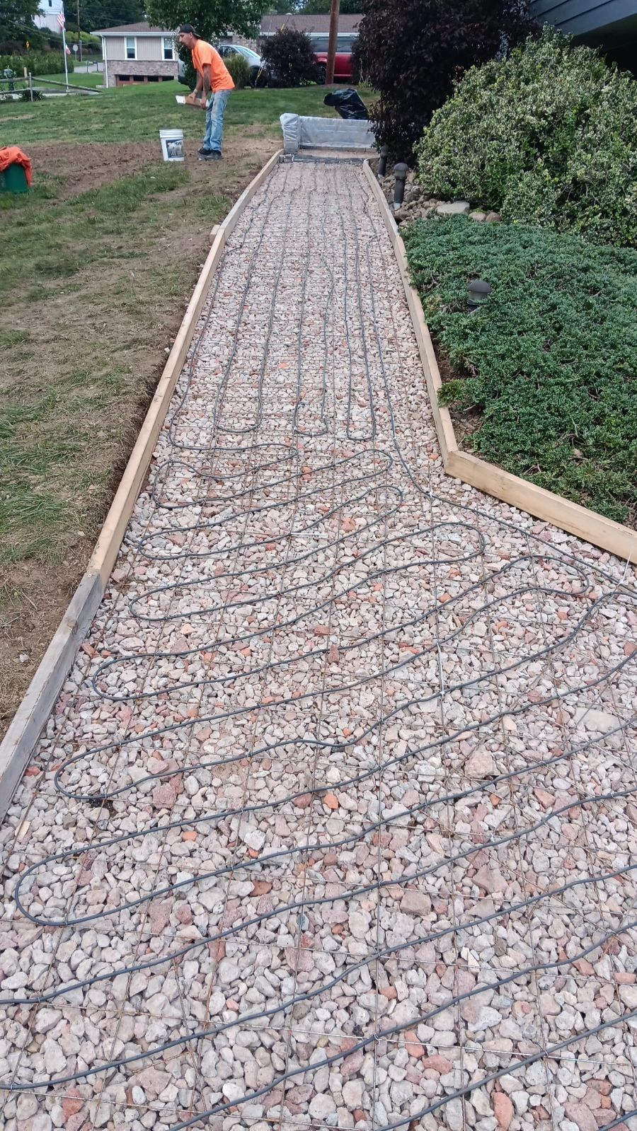 Gravel walkway under construction beside a lawn and bushes, with workers in the background