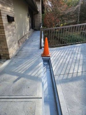 Orange cone marking a narrow ramp beside a building, with metal railing and outdoor walkway shadows