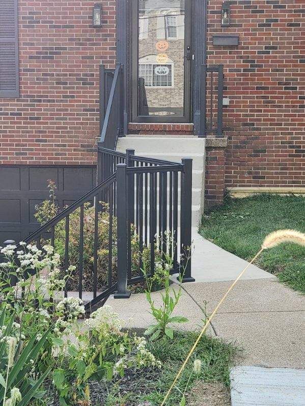 Brick house entrance with black railings, short ramp, and concrete walkway leading to the front door