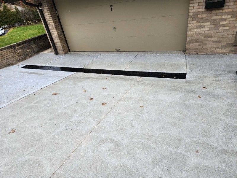 Concrete driveway with a long black drainage grate in front of a garage door.