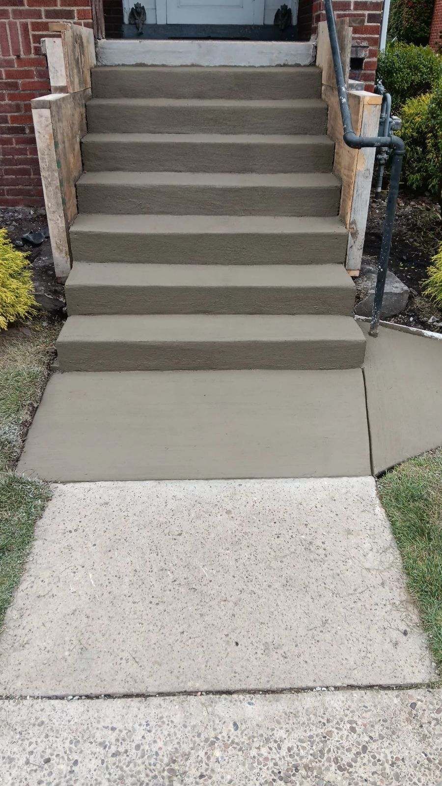 Concrete front steps leading to a porch, with a small ramp on the right side.
