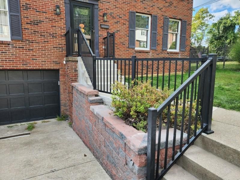 Brick townhouse entrance with black railings, steps, and a small front planter beside a garage.
