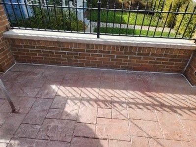 Brick patio beside a low brick wall and black metal fence, with strong sun-cast shadows.