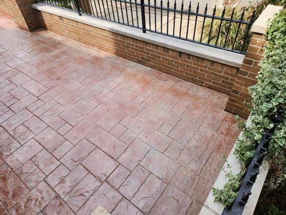 Brick patio beside a low brick wall and black metal fence, with a leafy shrub at the edge.