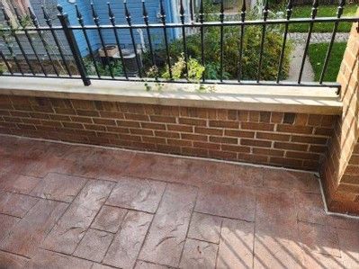 Brick patio with tiled floor, low wall, and black metal railing overlooking water and greenery