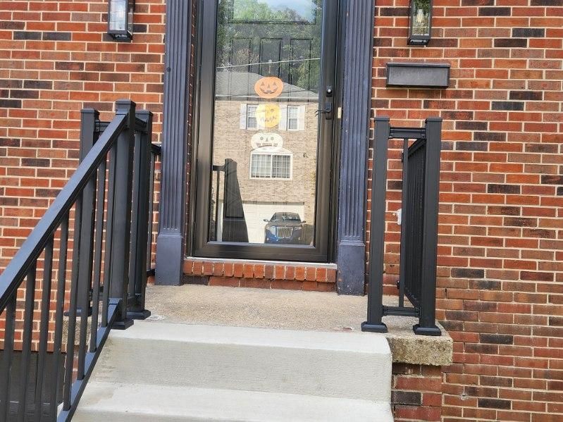 Front steps to a brick house with black railings and a glass front door reflecting the street.