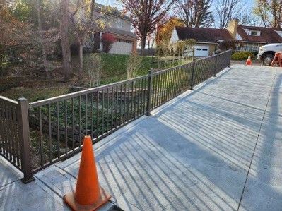 Concrete ramp with black railing beside a grassy ditch, orange traffic cone in foreground, houses in background