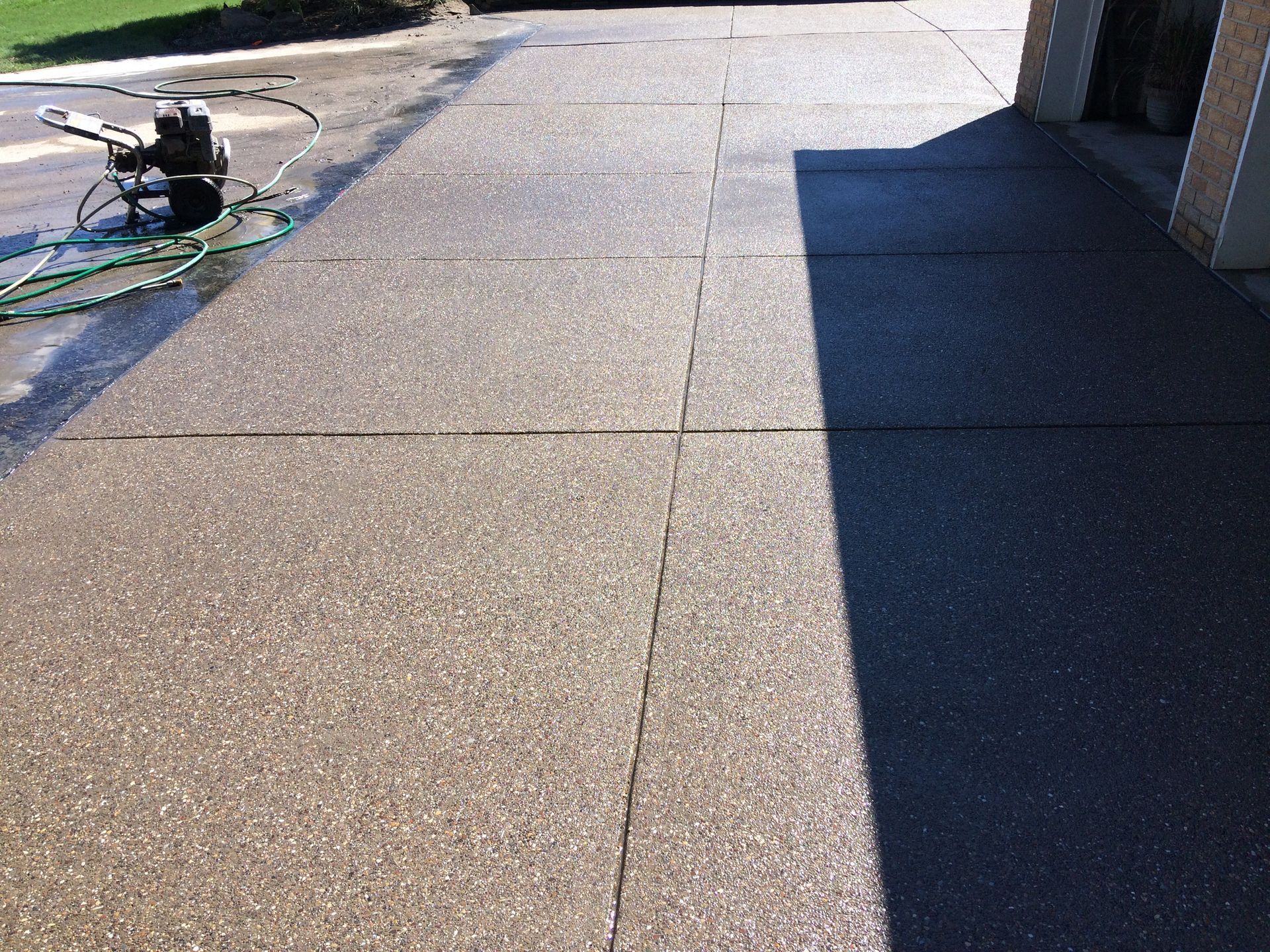 Concrete sidewalk beside a building, with a bicycle and tools on the left in bright sunlight.