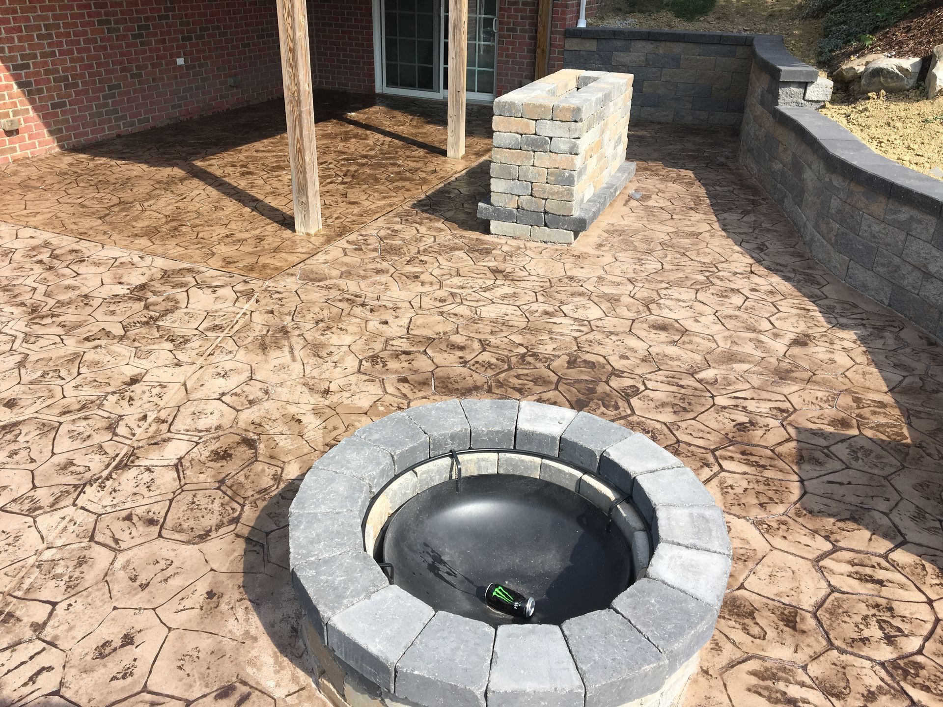 Circular fire pit with gray stone ring in a landscaped yard with brick patio and stone wall