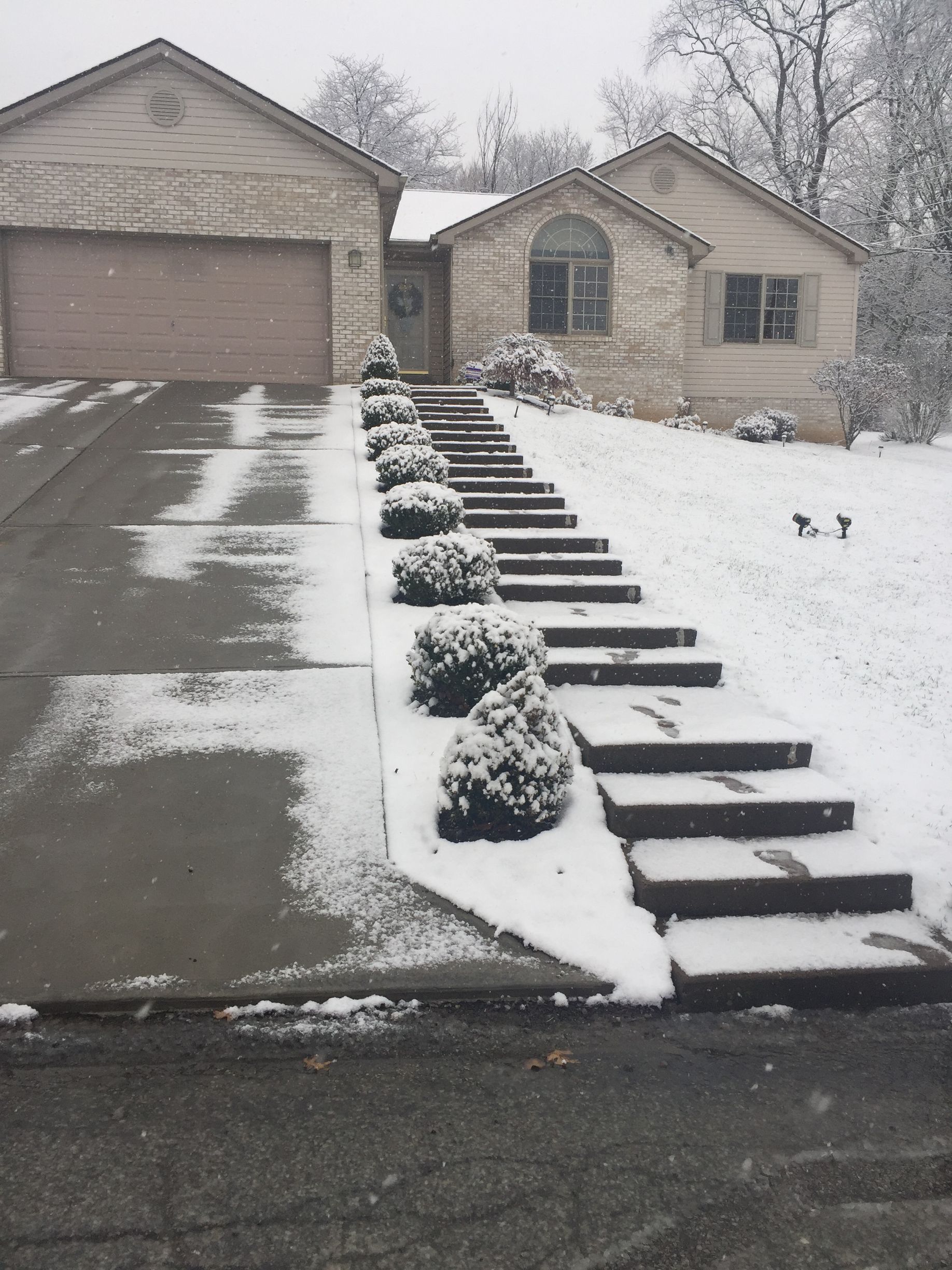 Snowy suburban driveway and front steps leading to a beige house with a garage.