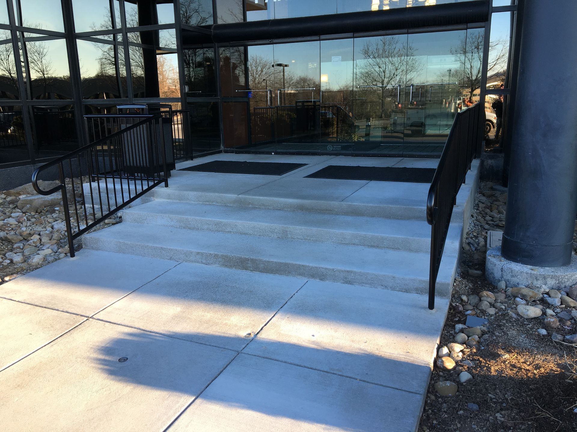 Concrete steps with black railings leading to a glass building entrance in winter sunlight