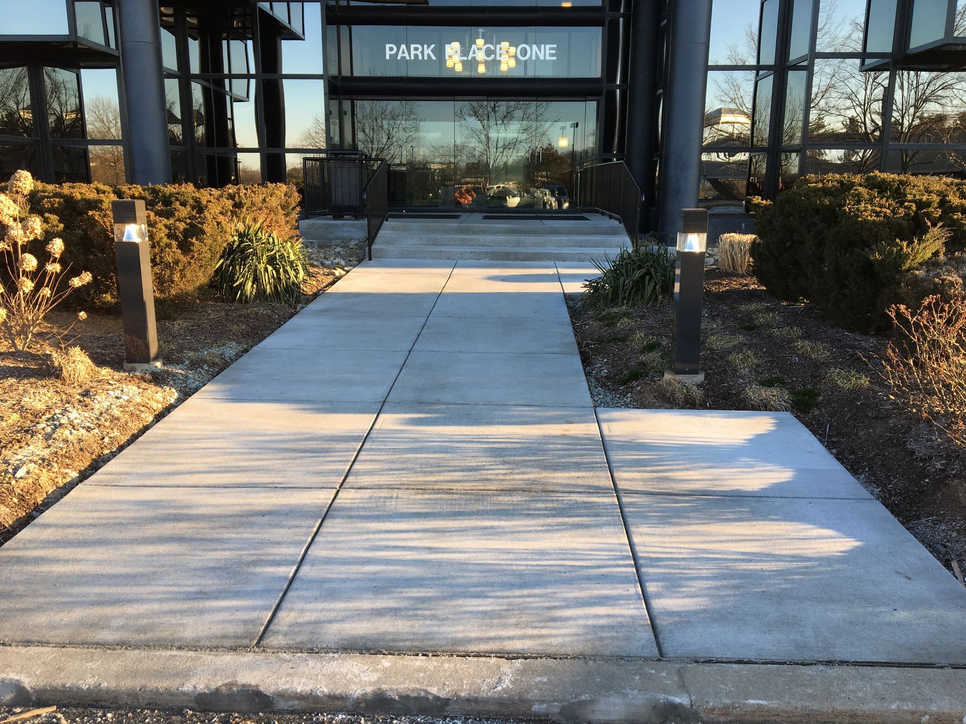 Walkway leading to a building entrance with glass doors and winter landscaping