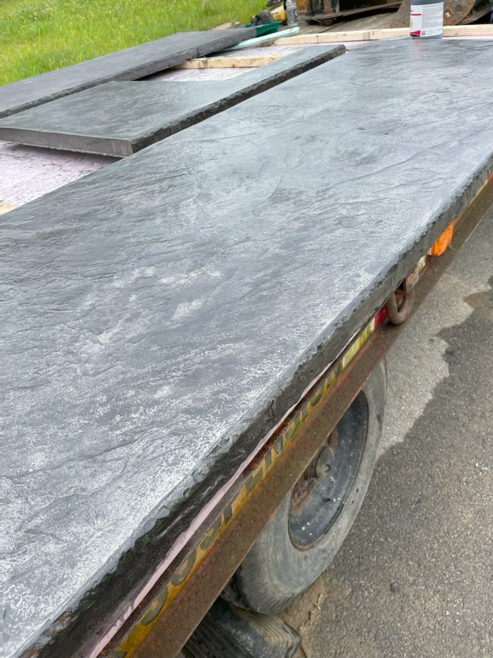 Large dark stone slab on a trailer, with another slab behind it beside a road