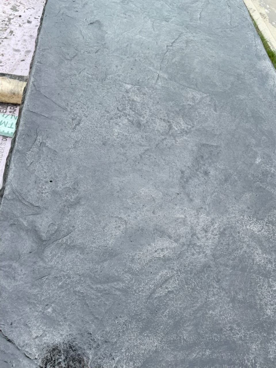 Dark gray concrete sidewalk slab with faint cracks and a metal drain edge at the side