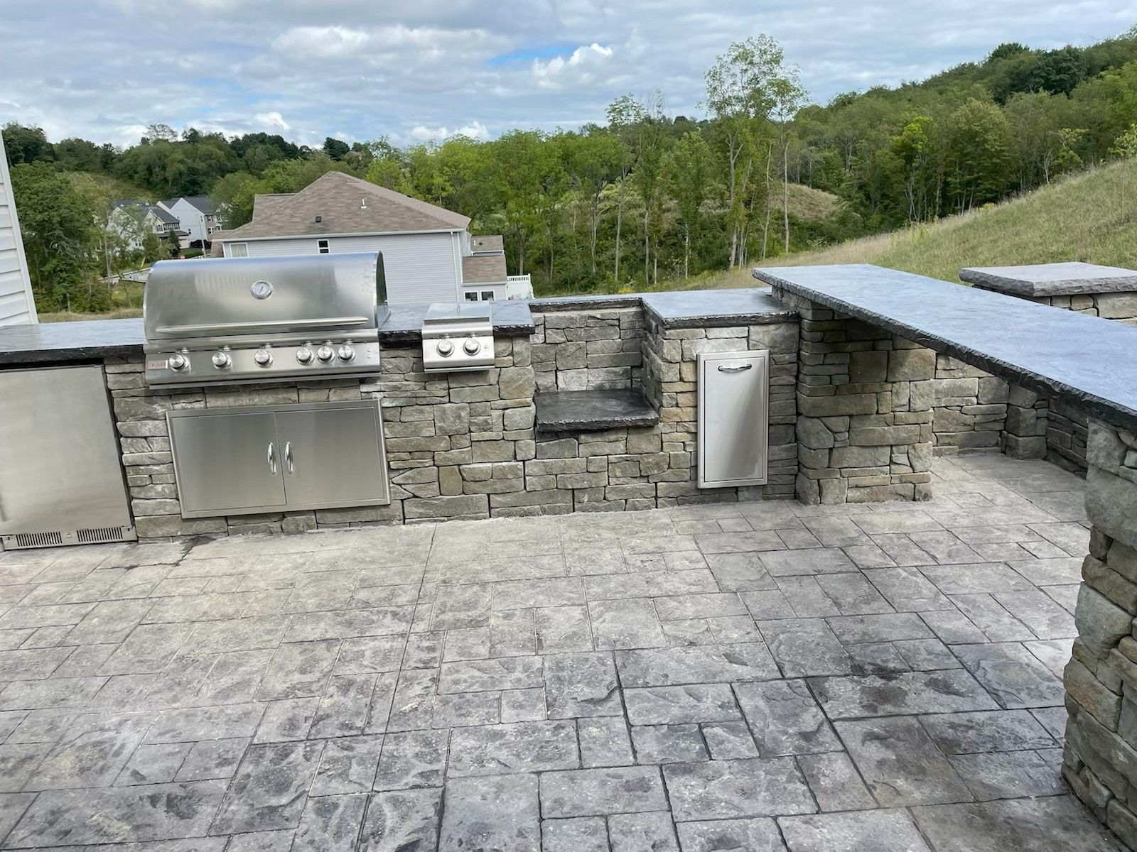Stone patio with built-in outdoor grill and counters overlooking a grassy landscape