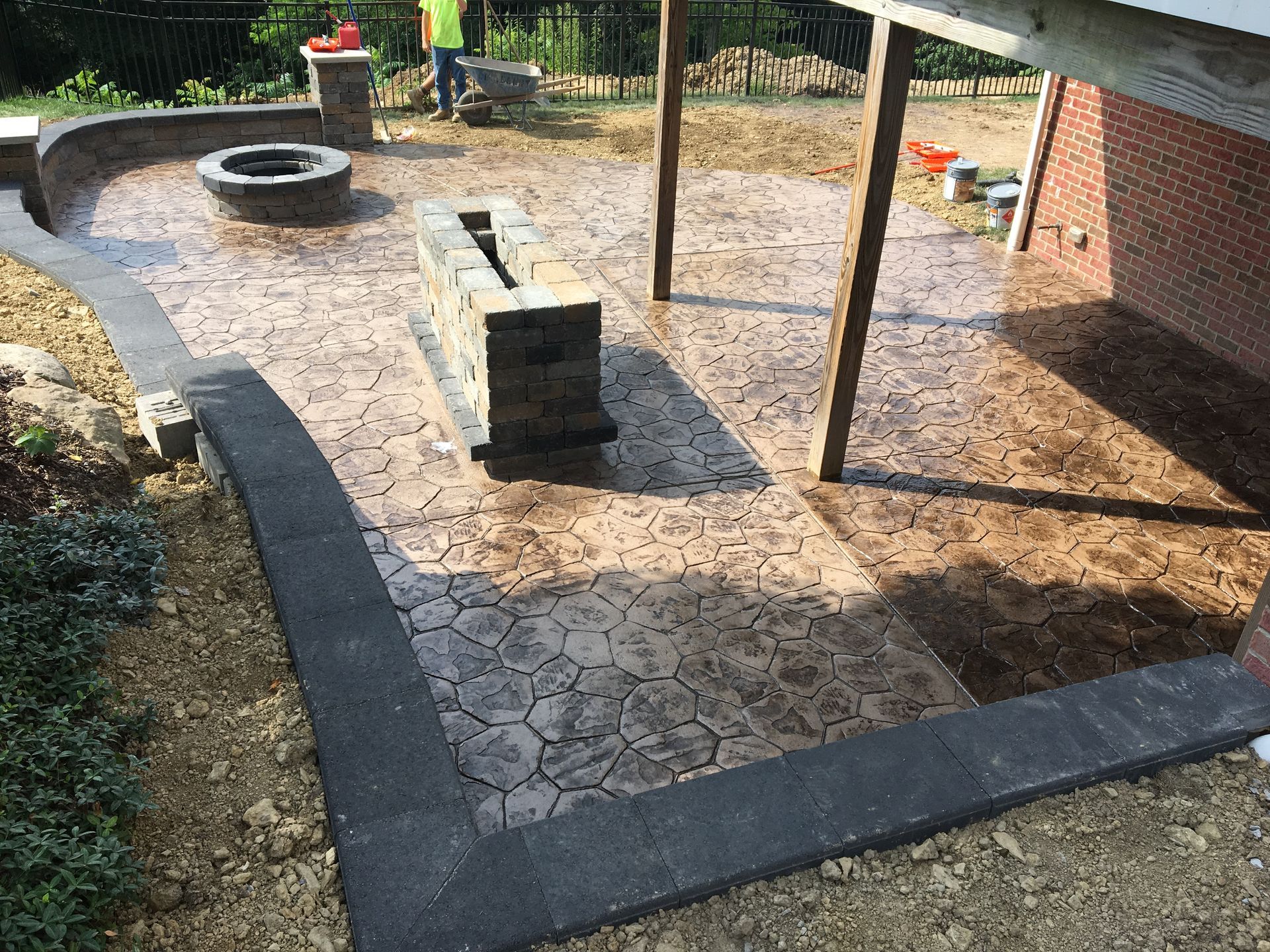 Backyard patio with stone paving, a circular fire pit, and a central concrete bench under a pergola.