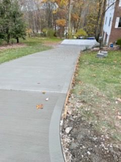 Fresh concrete driveway curving past a house, with grass and trees on both sides.