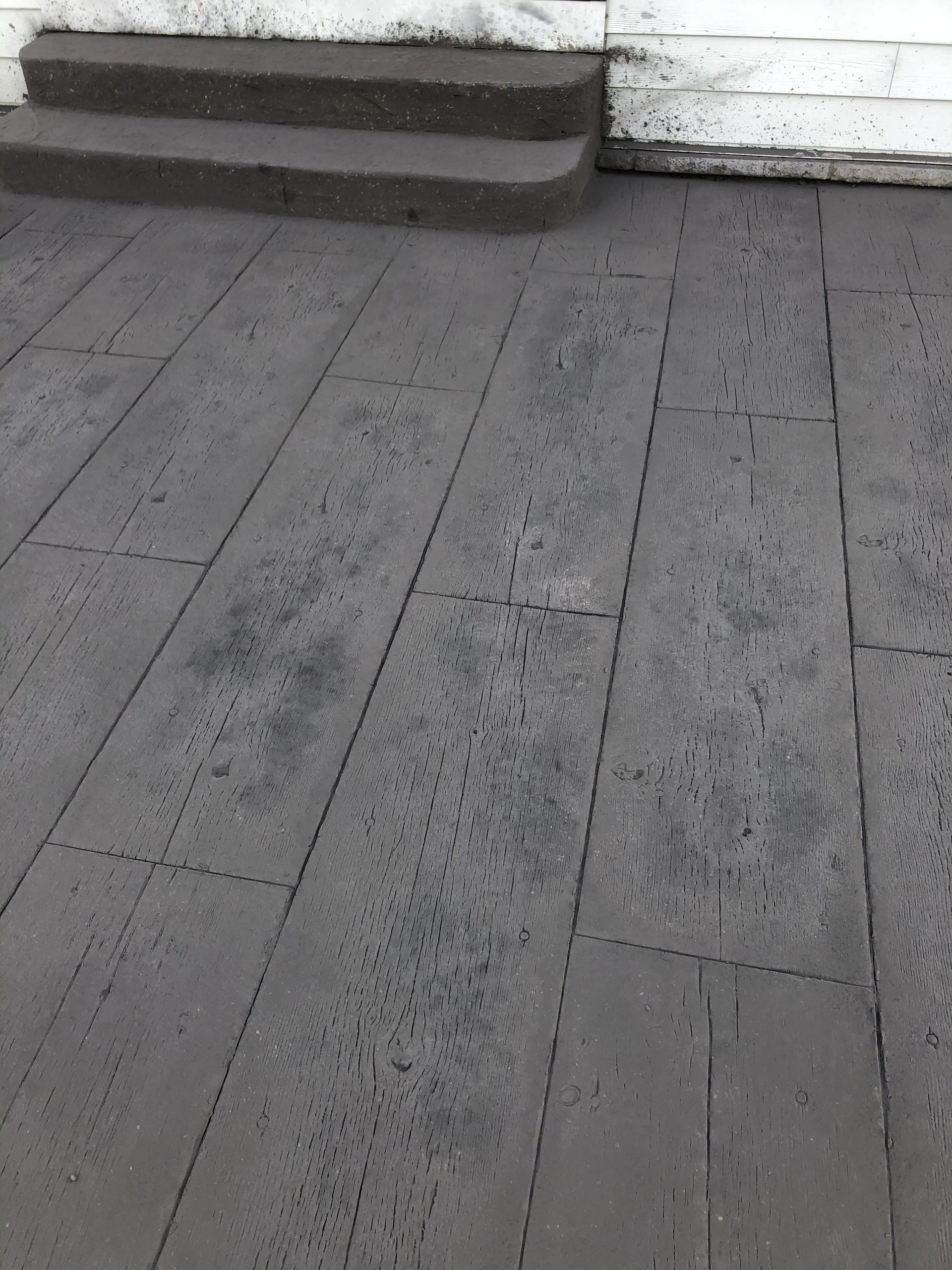 Gray wooden deck boards beside a white step and wall, with a slightly worn surface.