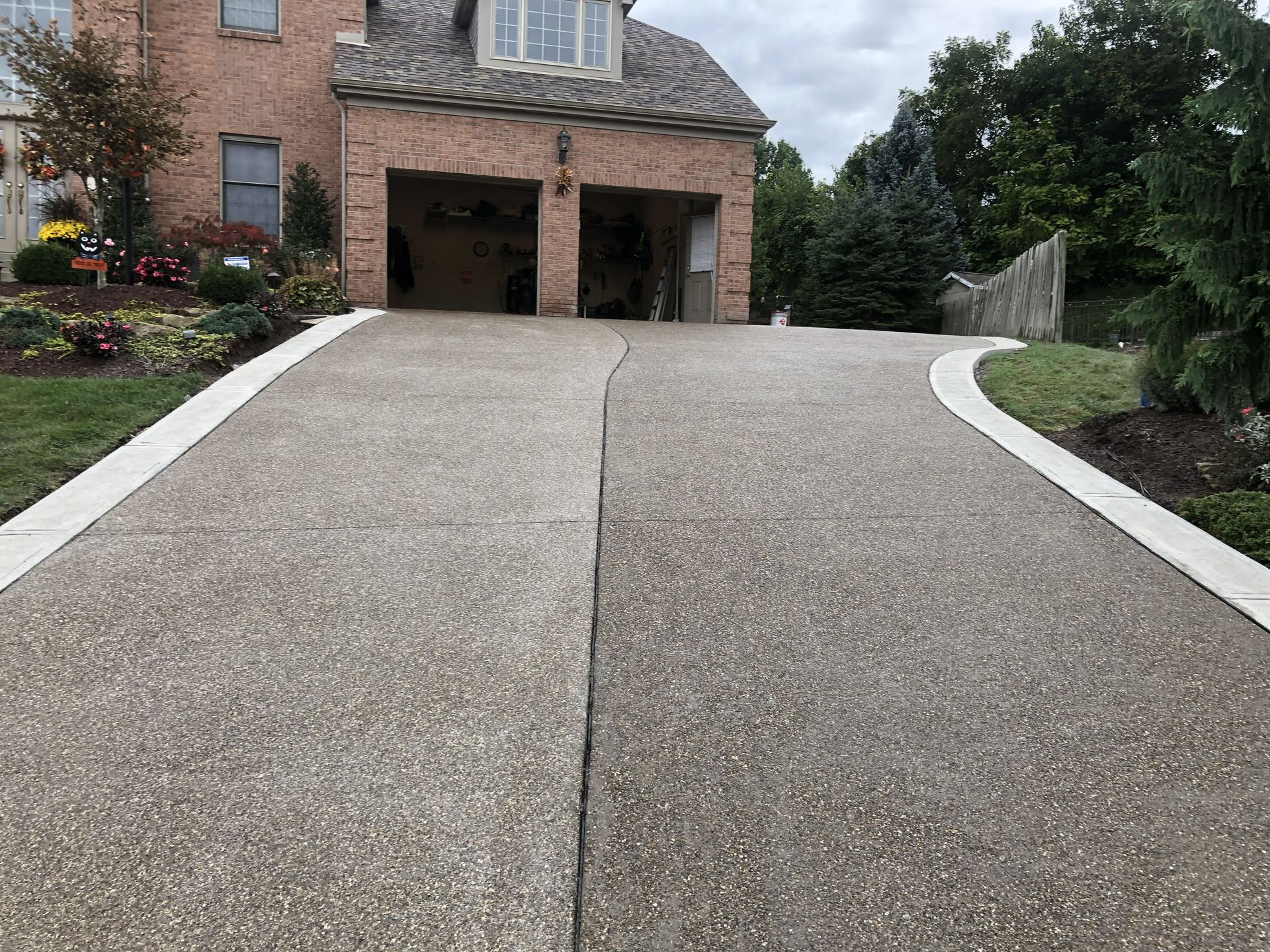 Long concrete driveway leading to a brick garage on a sloped front yard
