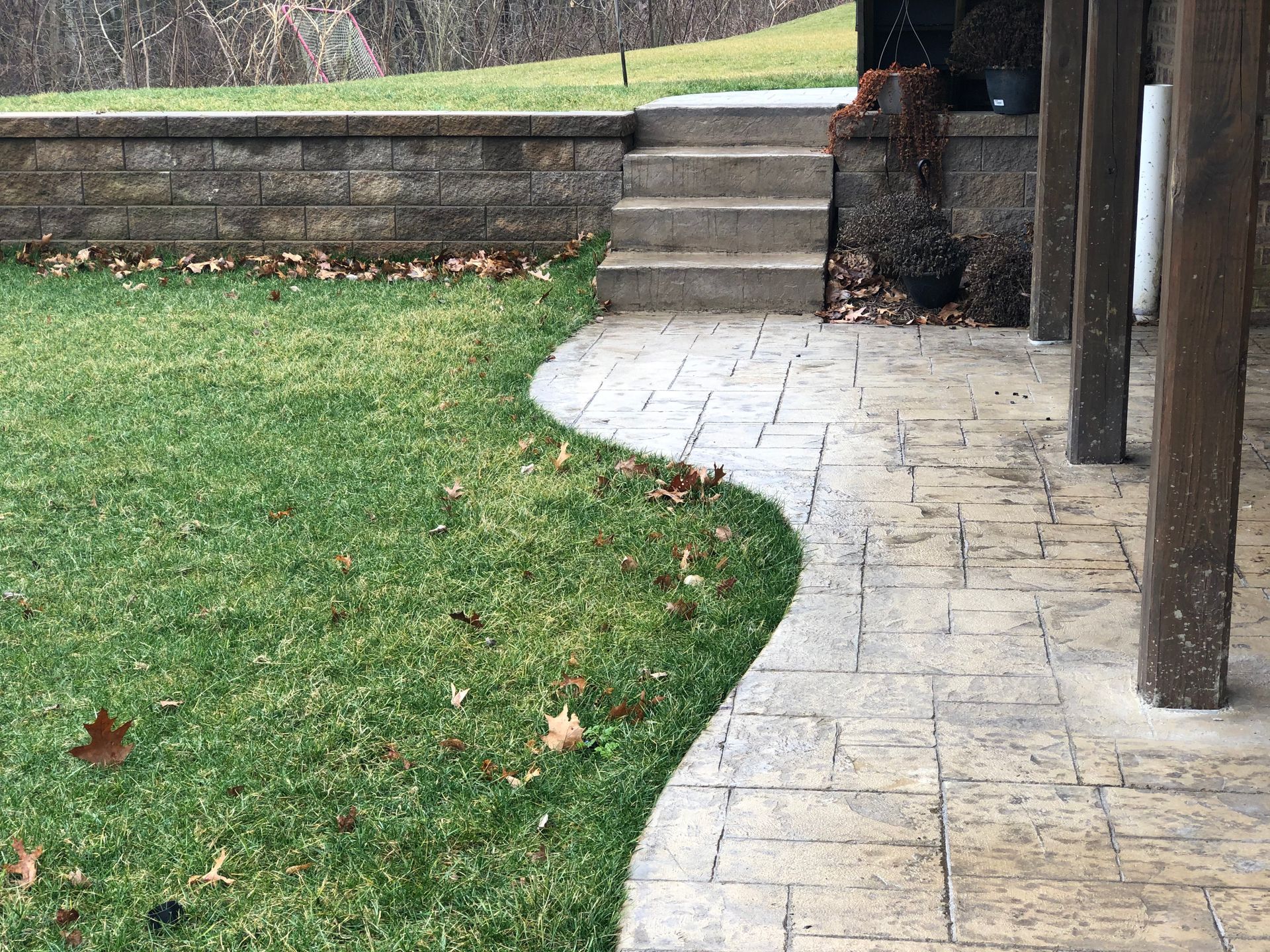Curved stone walkway beside a grassy yard, leading to steps and a wooden post