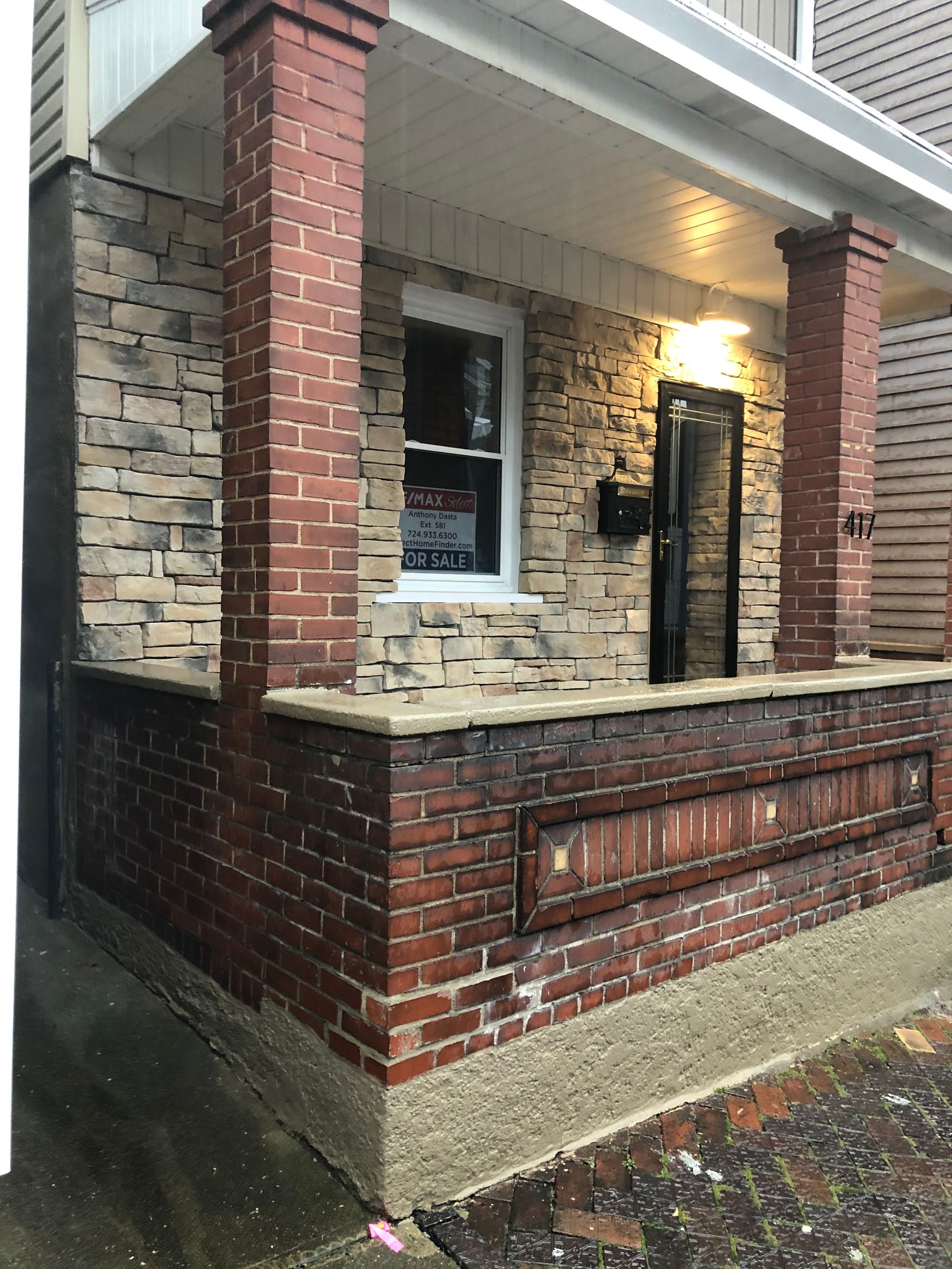 Brick front porch with stone wall, red columns, and a lit doorway under a covered overhang