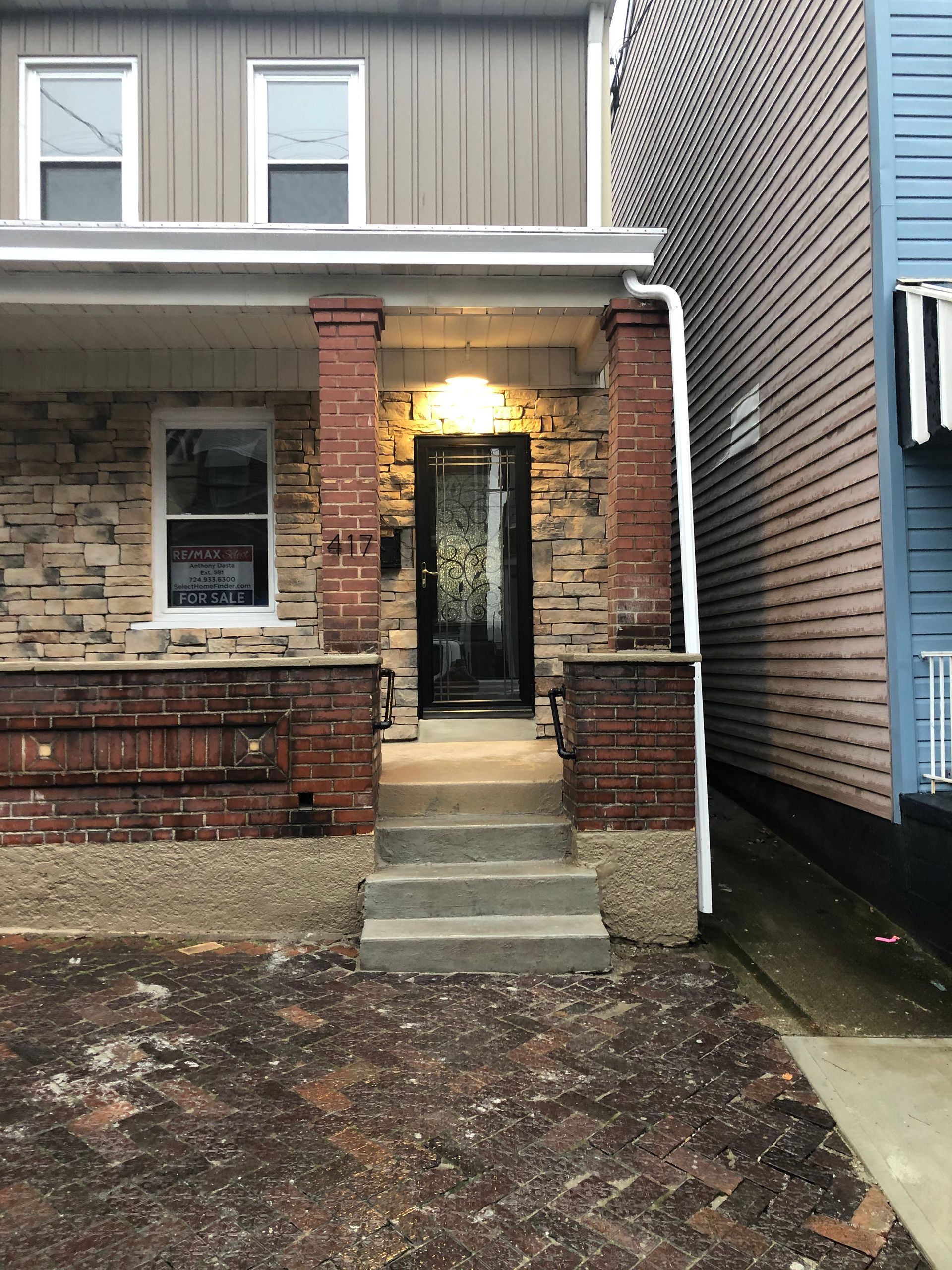 Brick townhouse entrance with lit doorway, concrete steps, and narrow front porch over wet ground