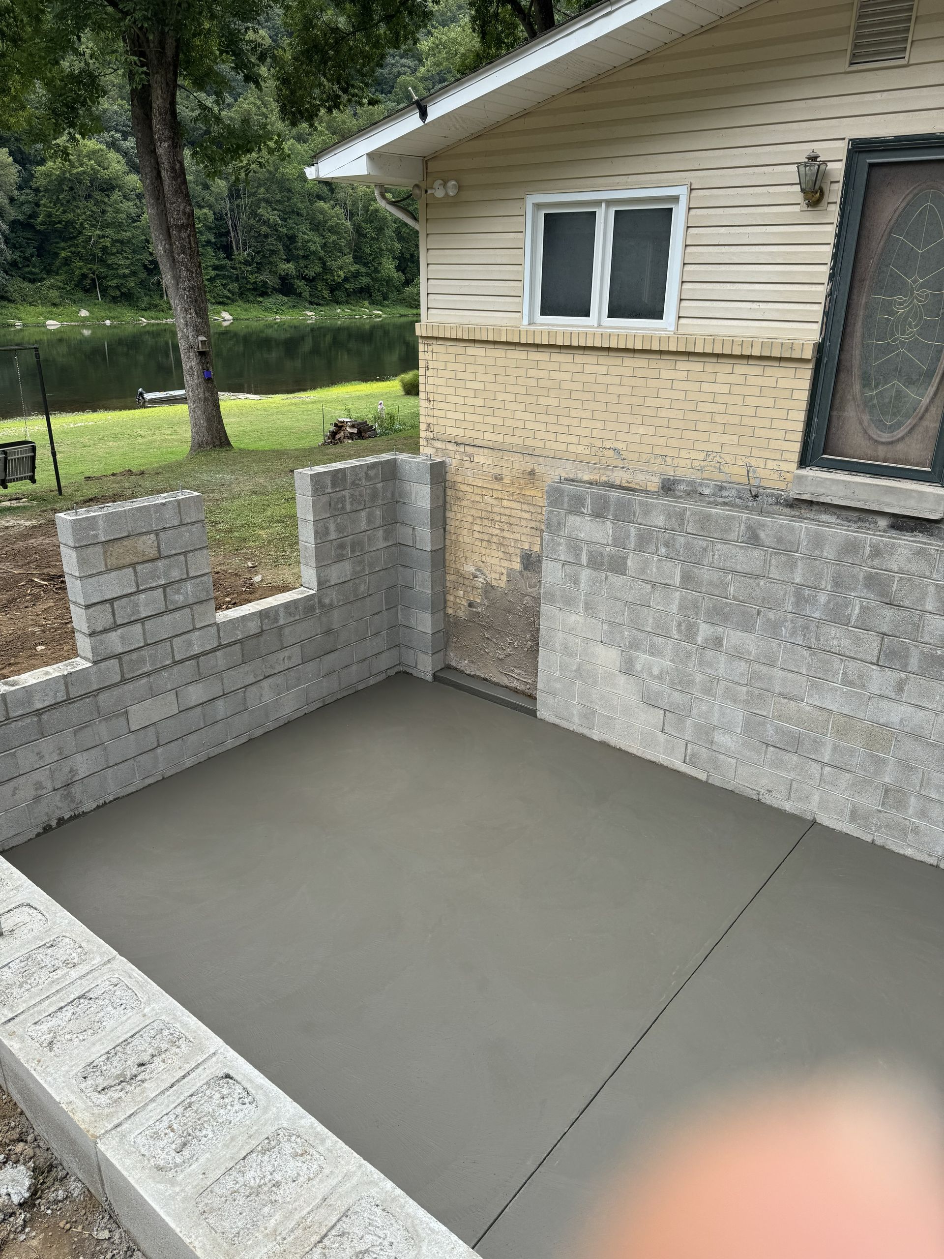 Fresh concrete patio enclosed by low brick walls beside a beige house with a window and door